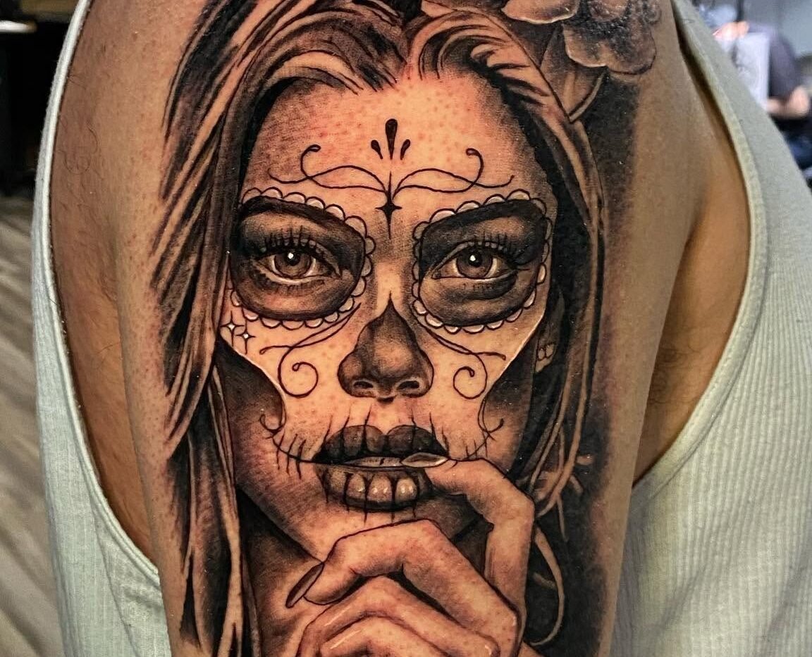 Black and grey Catrina portrait tattoo with a rose on the upper arm