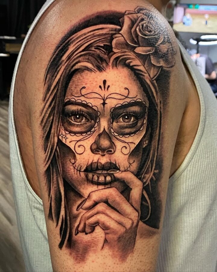 Black and grey Catrina portrait tattoo with a rose on the upper arm