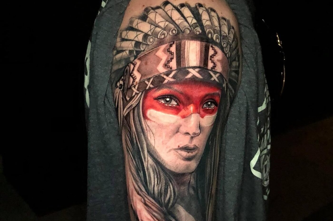 Portrait tattoo of a woman in a feathered headdress with red face paint on the upper arm