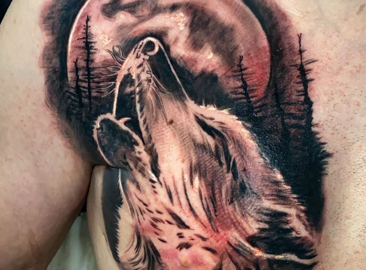 Black and grey howling wolf tattoo with moon and pine trees on the chest