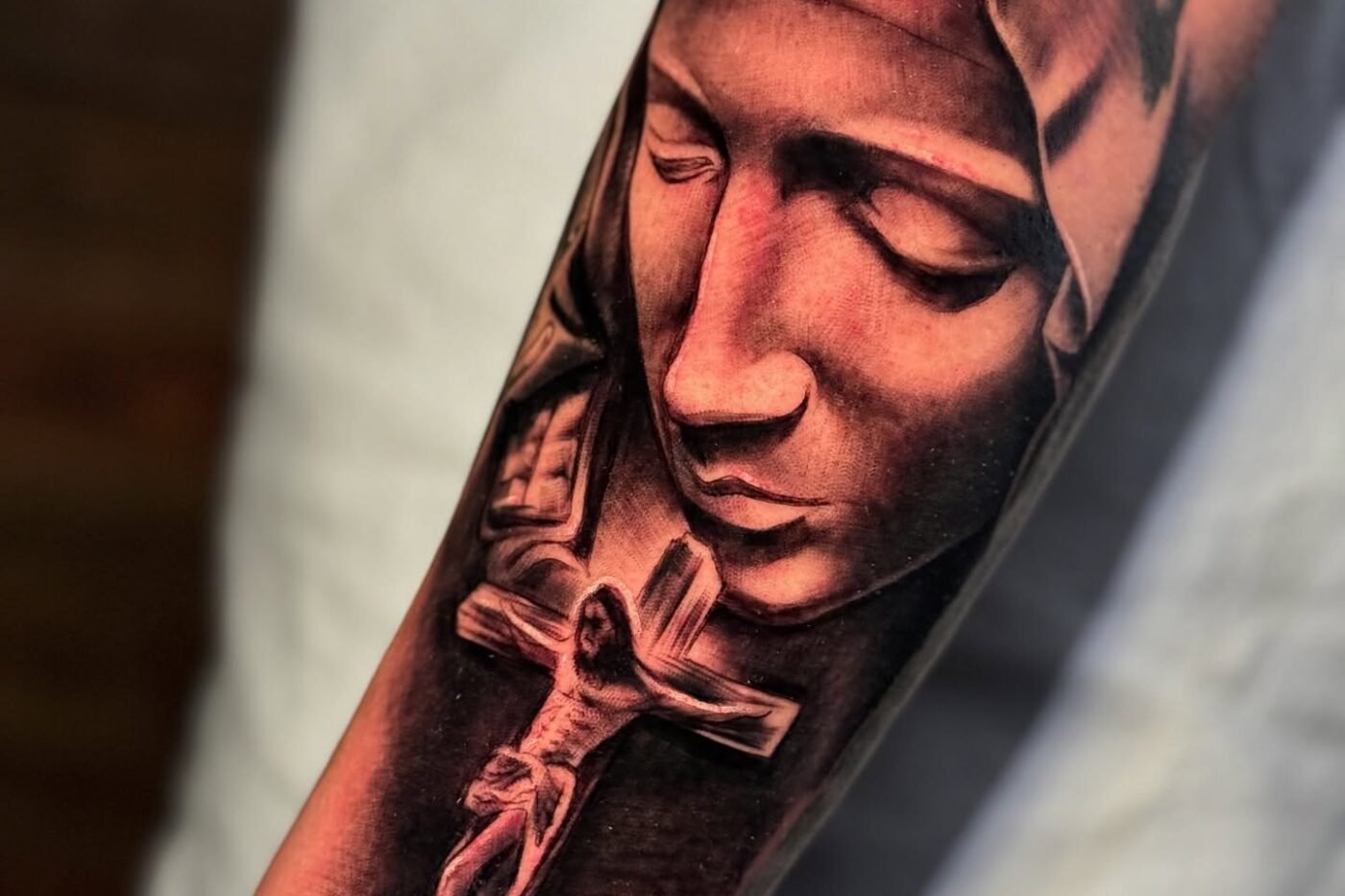 Black and grey tattoo of the Pieta with a crucifix on the forearm